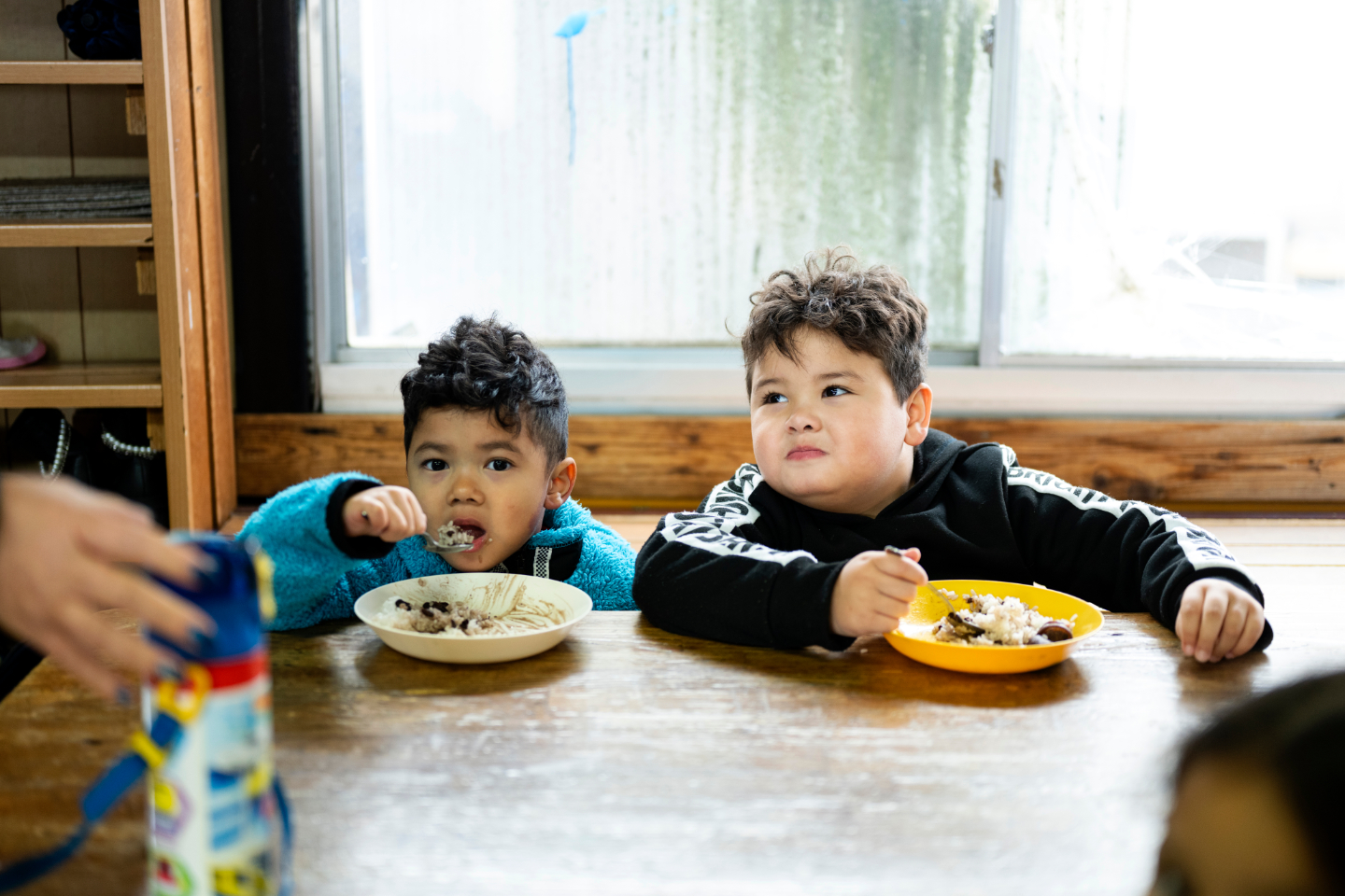 【写真】幼い子どもたちがスプーンを手にしながら、食卓で食事をしている。