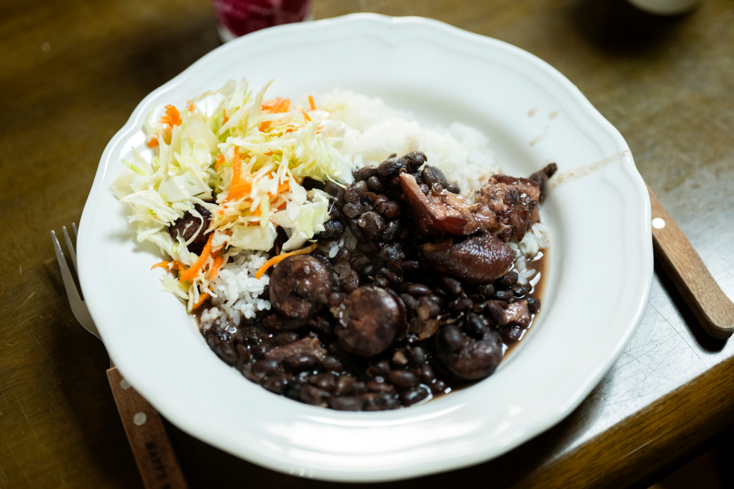 【写真】白い皿に黒豆の煮込みとソーセージ、ご飯、サラダが盛り付けられている