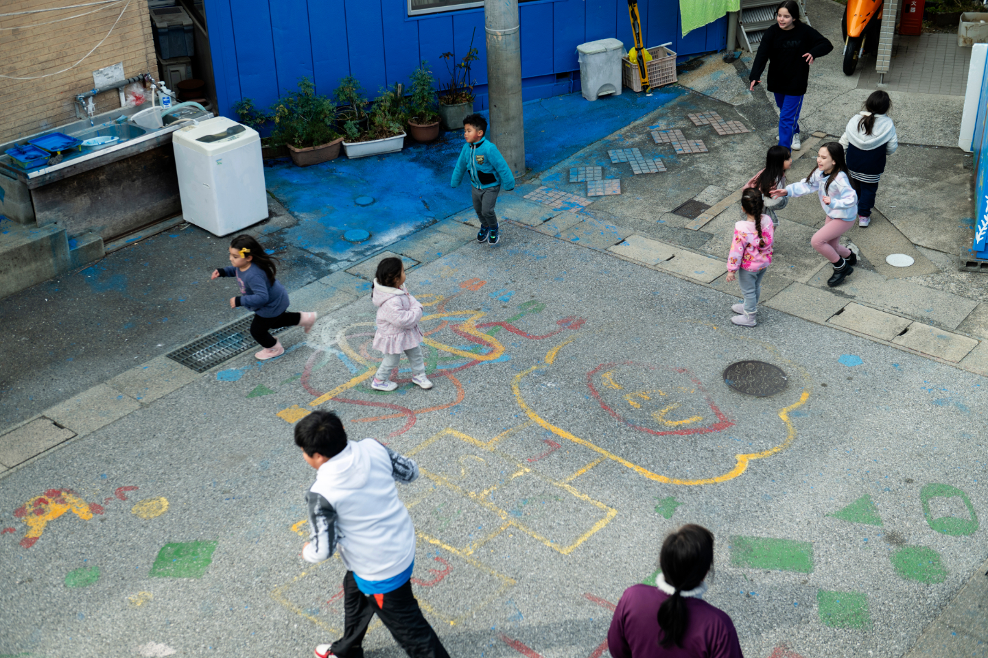 【写真】上から見下ろした路地で、子どもたちが地面に描かれたカラフルな絵の上を走り回って遊んでいる