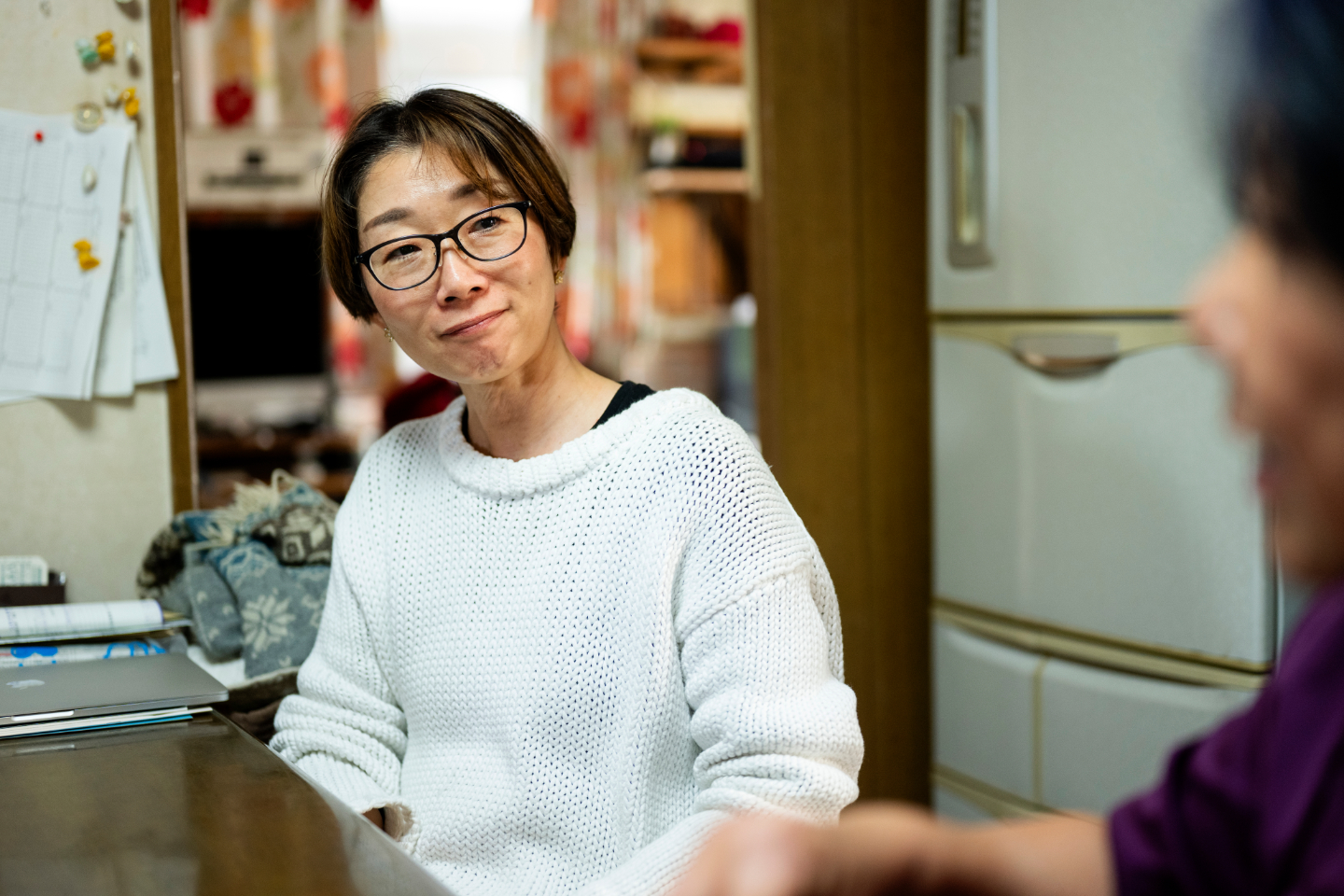 【写真】白いセーターを着た女性が、耳を傾けながら微笑んでいる