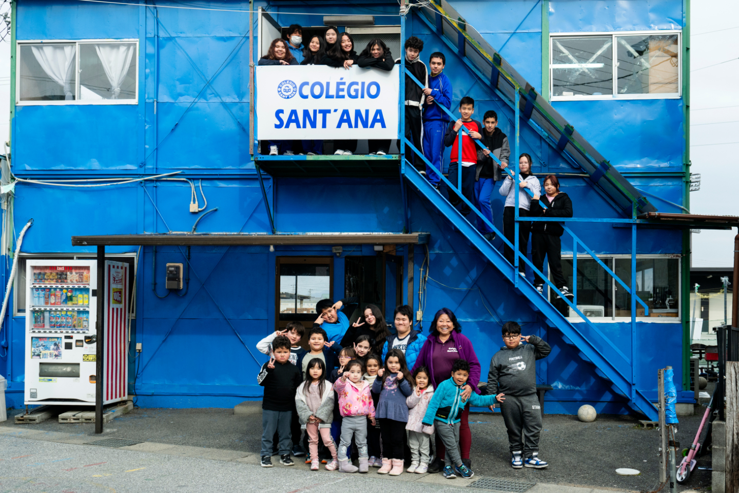 青い建物の前に、子どもたちと大人たちが集まった集合写真