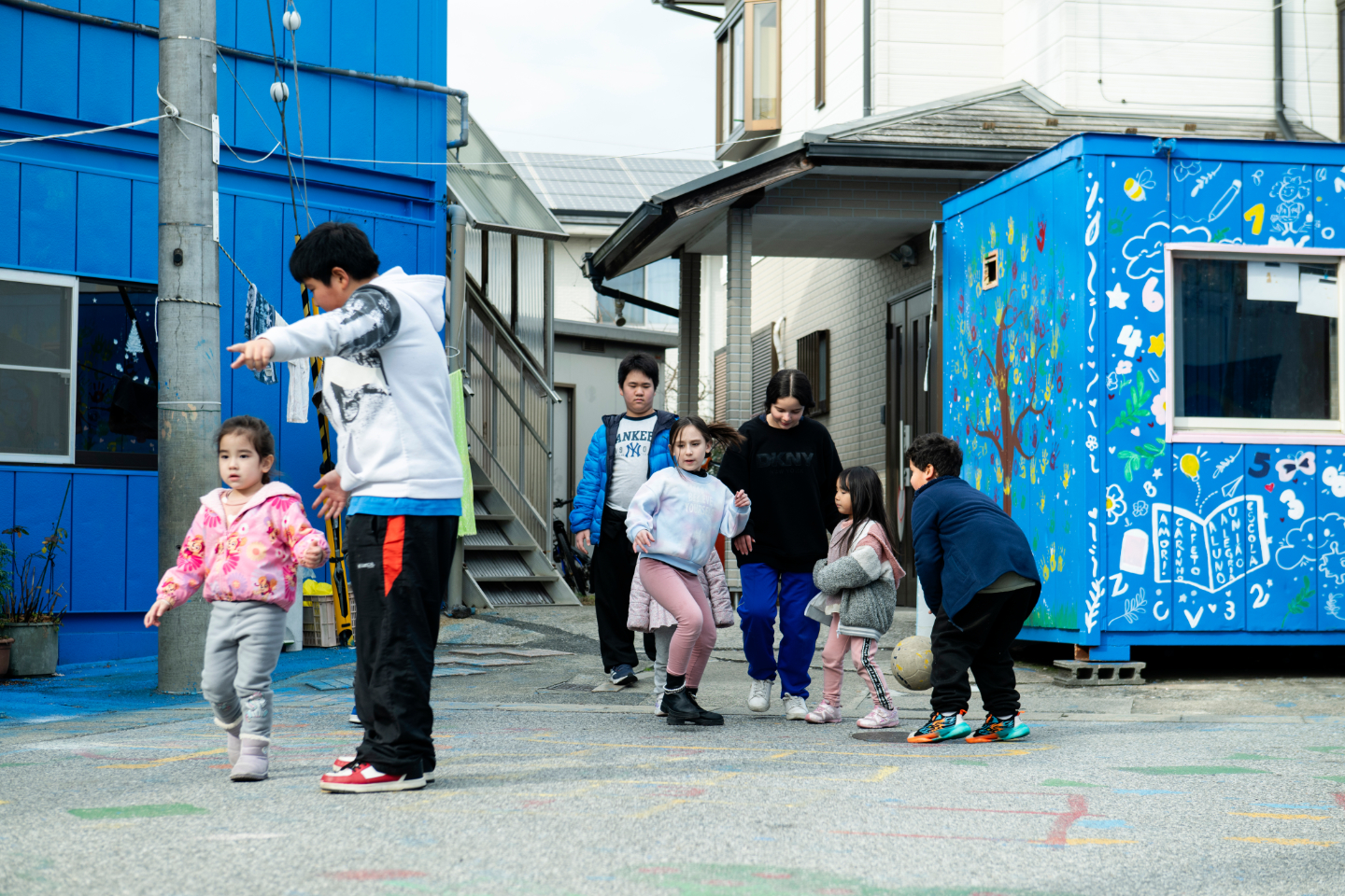 【写真】青く塗られた建物の前で、さまざまな年齢の子どもたちが遊んでいる