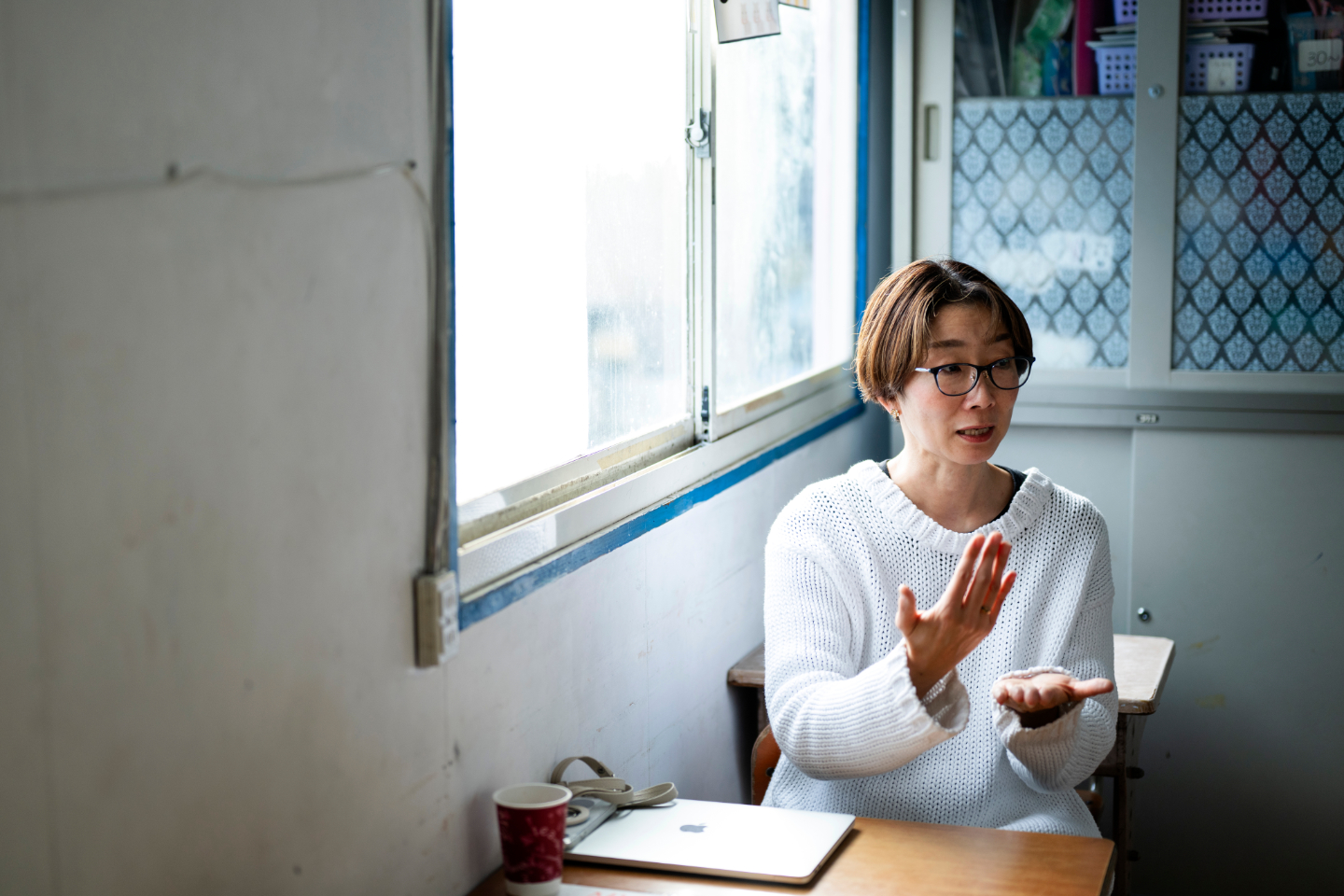 【写真】教室の窓際で、柳田さんが身振りを交えながら話しているインタビュー風景