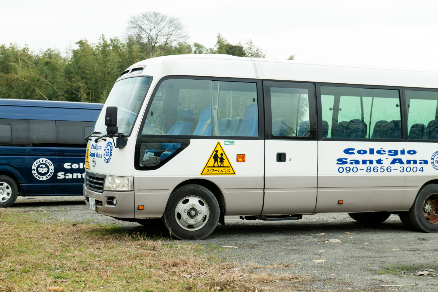 【写真】校庭脇に停車するスクールバス。車体には学校名のロゴが描かれている