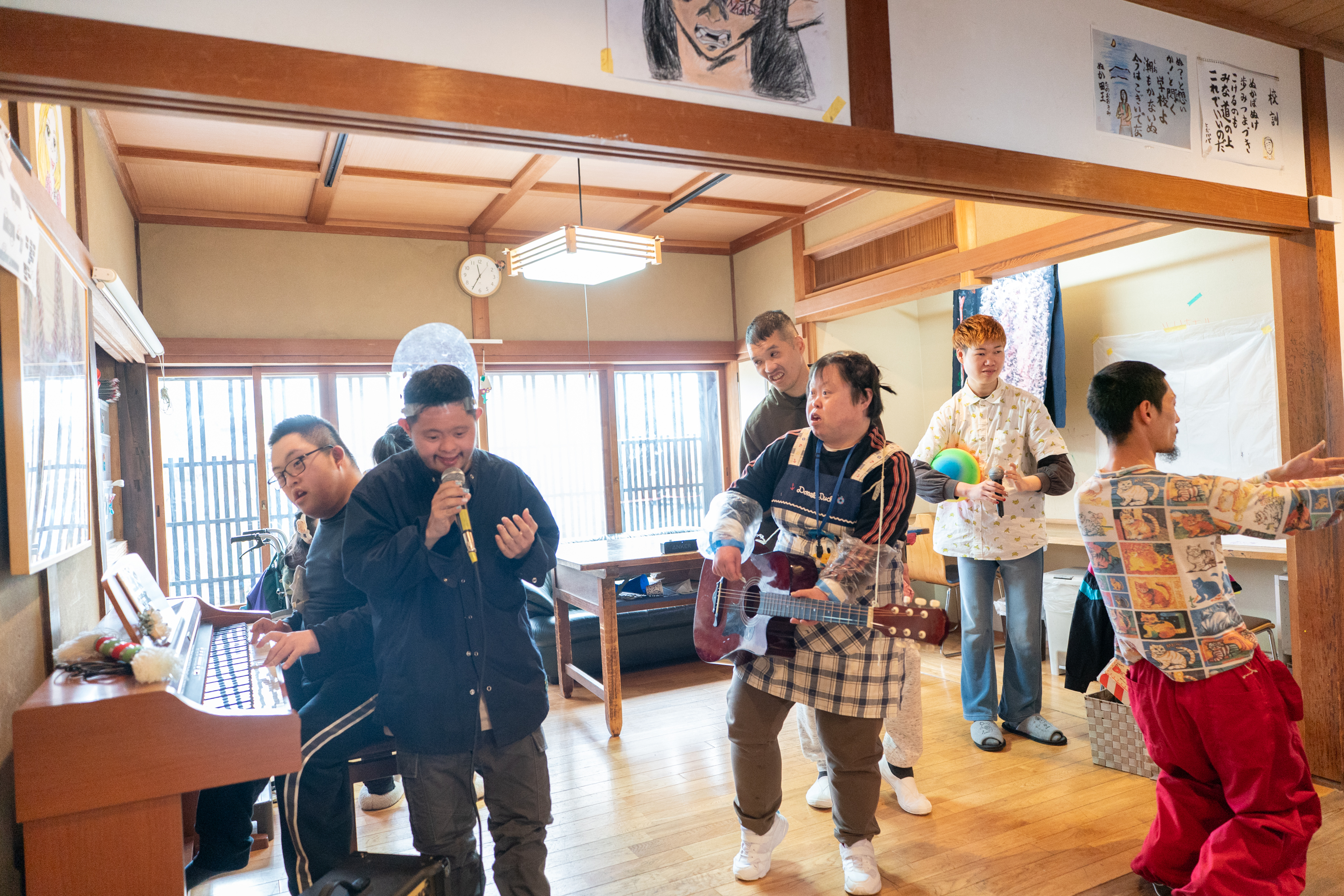 【写真】部屋の一室で、バンド演奏をする人たち、ギター、ボーカル、ピアノ、踊り子、賑やかしがいる