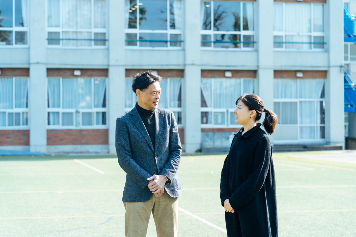 【写真】芝生の運動場で、向き合って語り合う平尾さんと野口さん