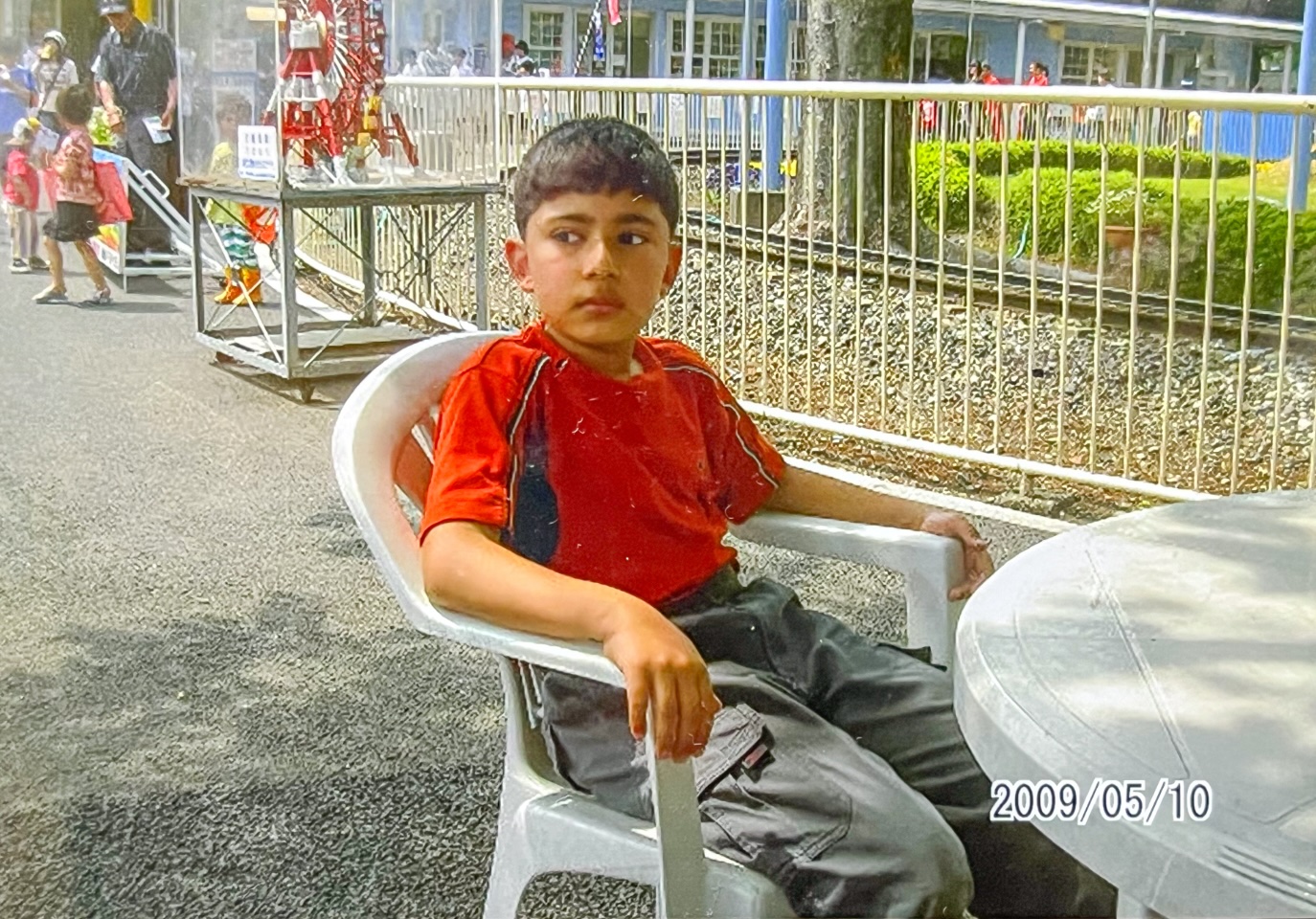 【写真】遊園地のような場所で、ベンチに腰掛ける少年