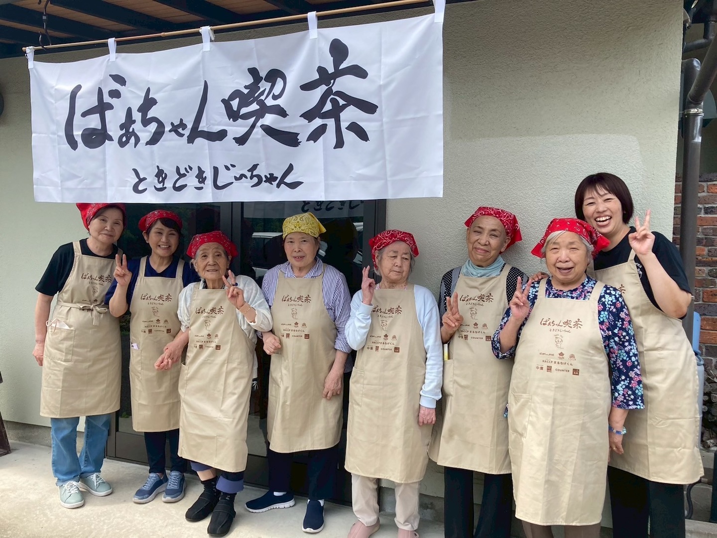 ばあちゃん喫茶ののれんの前で撮影されたばあちゃんたちの集合写真