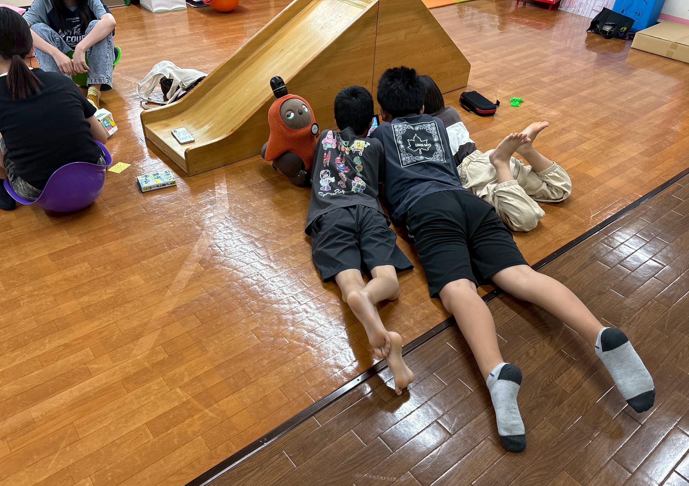【写真】さまざまな年齢の子が床に寝そべっている。そばには、ロボットのラボット