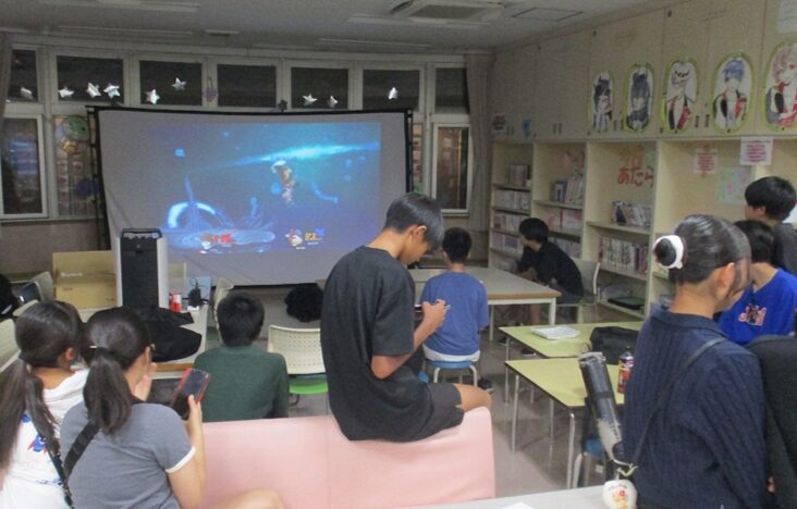 【写真】外が暗いなか、部屋の大きなモニターで映画を見る子どもたち