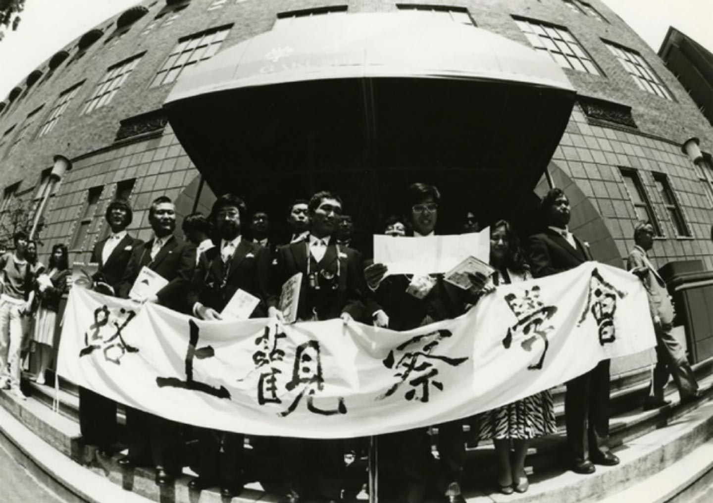 「路上観察学会」という幟を掲げ、神田の東京学士会館前に集まっているメンバーたちのモノクロ写真。
