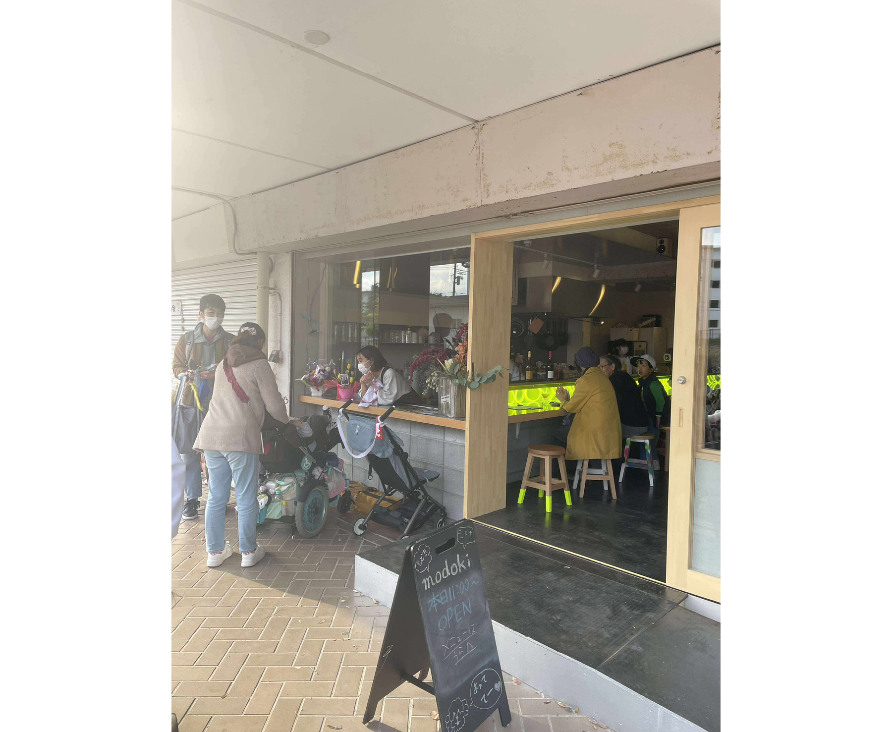 【写真】お店の軒下から、大きなガラス窓やガラス扉ごしに店内が見える。外にはベビーカーが並ぶ