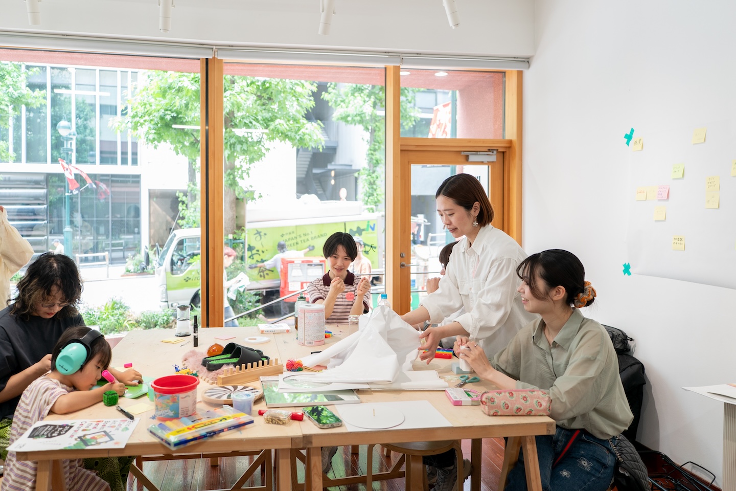 大きなひとつの机の上で作業する大人たちと何かを書いているようすの子どもが一緒にいる