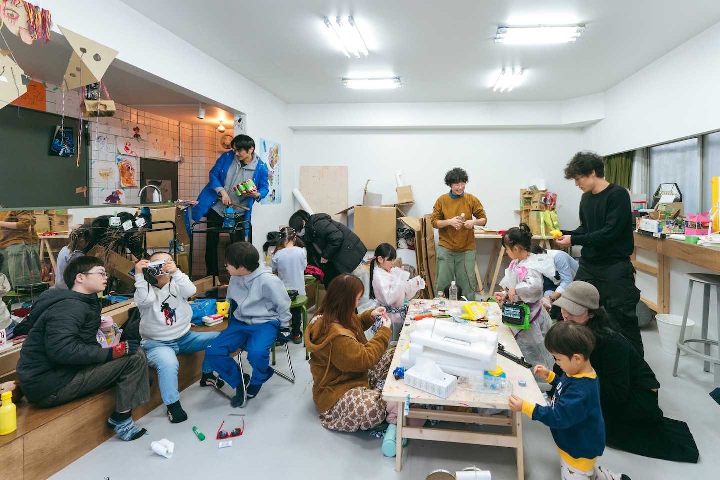ひとつの部屋で、何かをつくっている様子の大人、子ども、カメラを構える子ども、いろんな人がいる