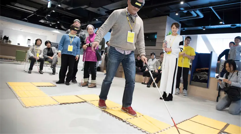 【写真】白杖をついた人が目隠しをされて歩いている
