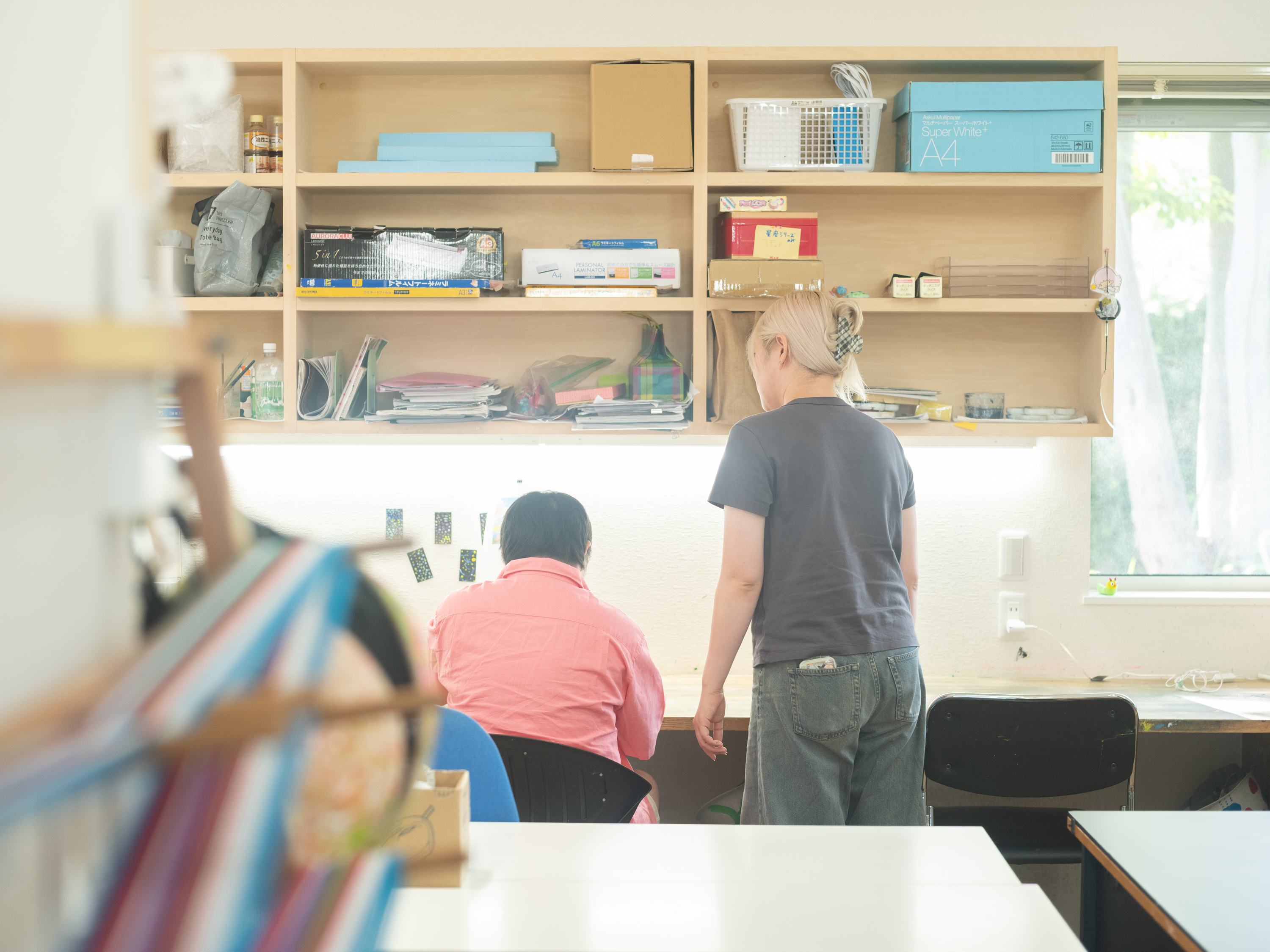 【写真】机の前で座っている人と、それをそばで見守る人